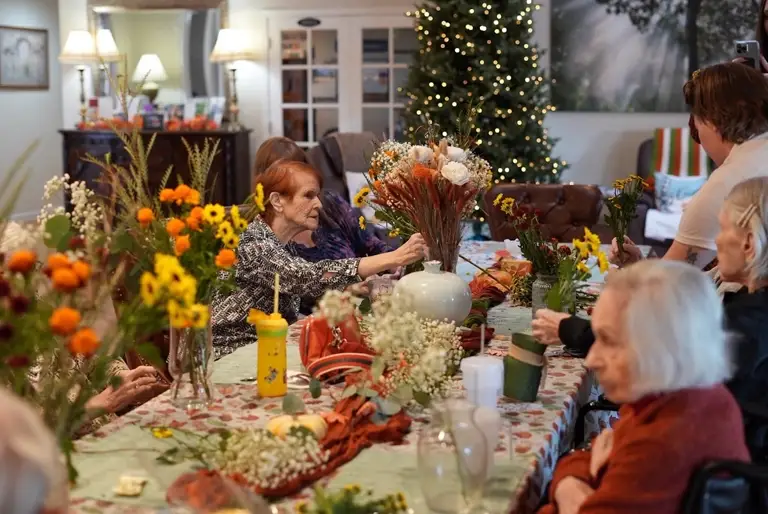 Residents arranging autumn flowers together around the dining table at Sweetwater Groves in Scottsdale